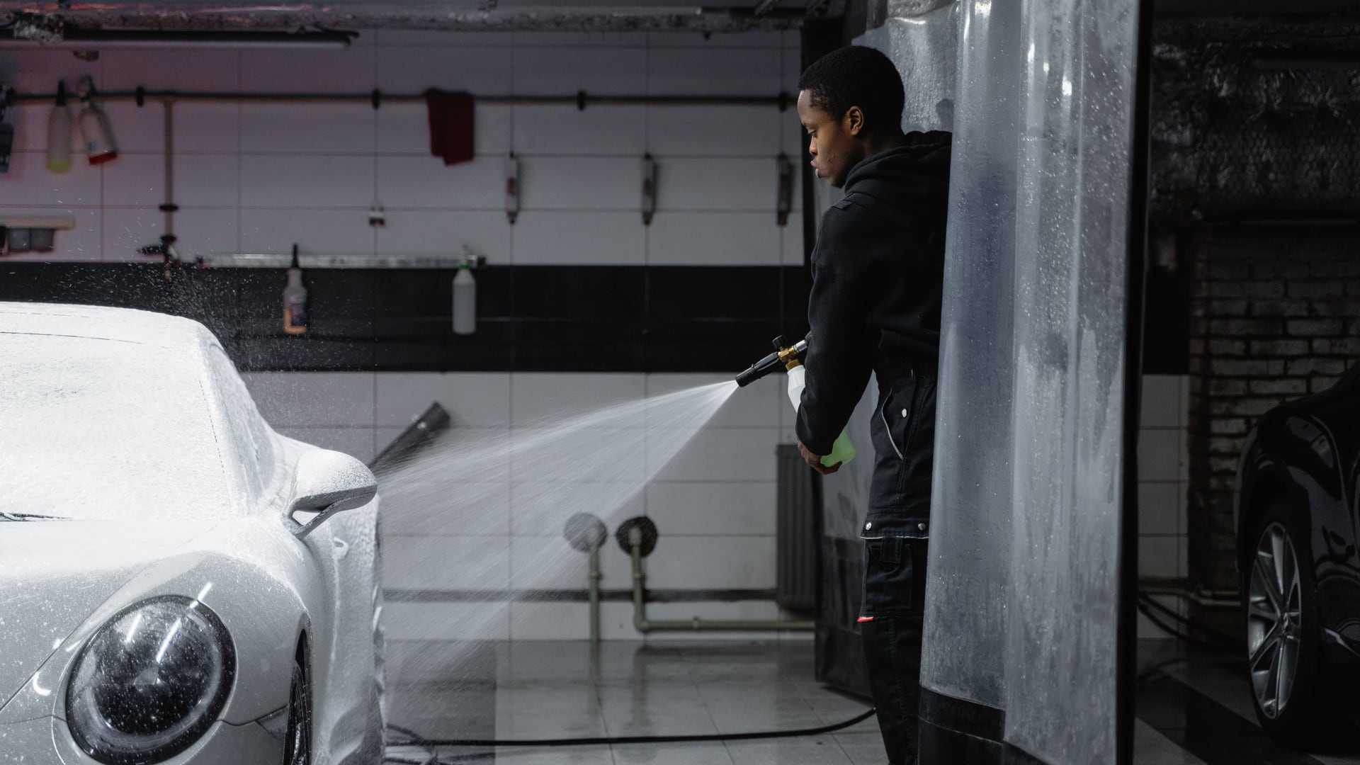 A detailer pressure-washing a white vehicle in a real work bay