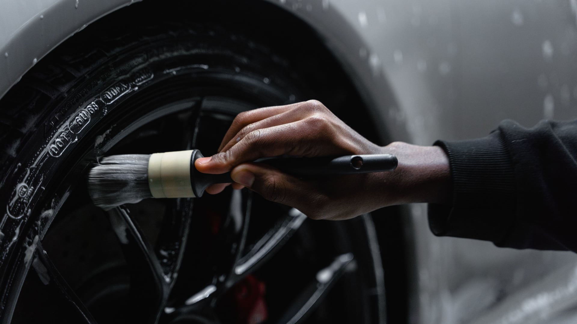 A detailer brushing a wet wheel face by hand